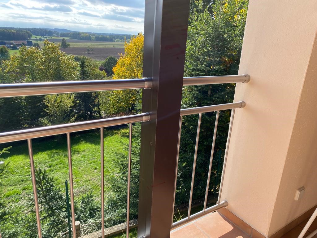 Edelstahl-Stabgeländer an einem Balkon mit Eckpfosten und Blick über Garten und Landschaft